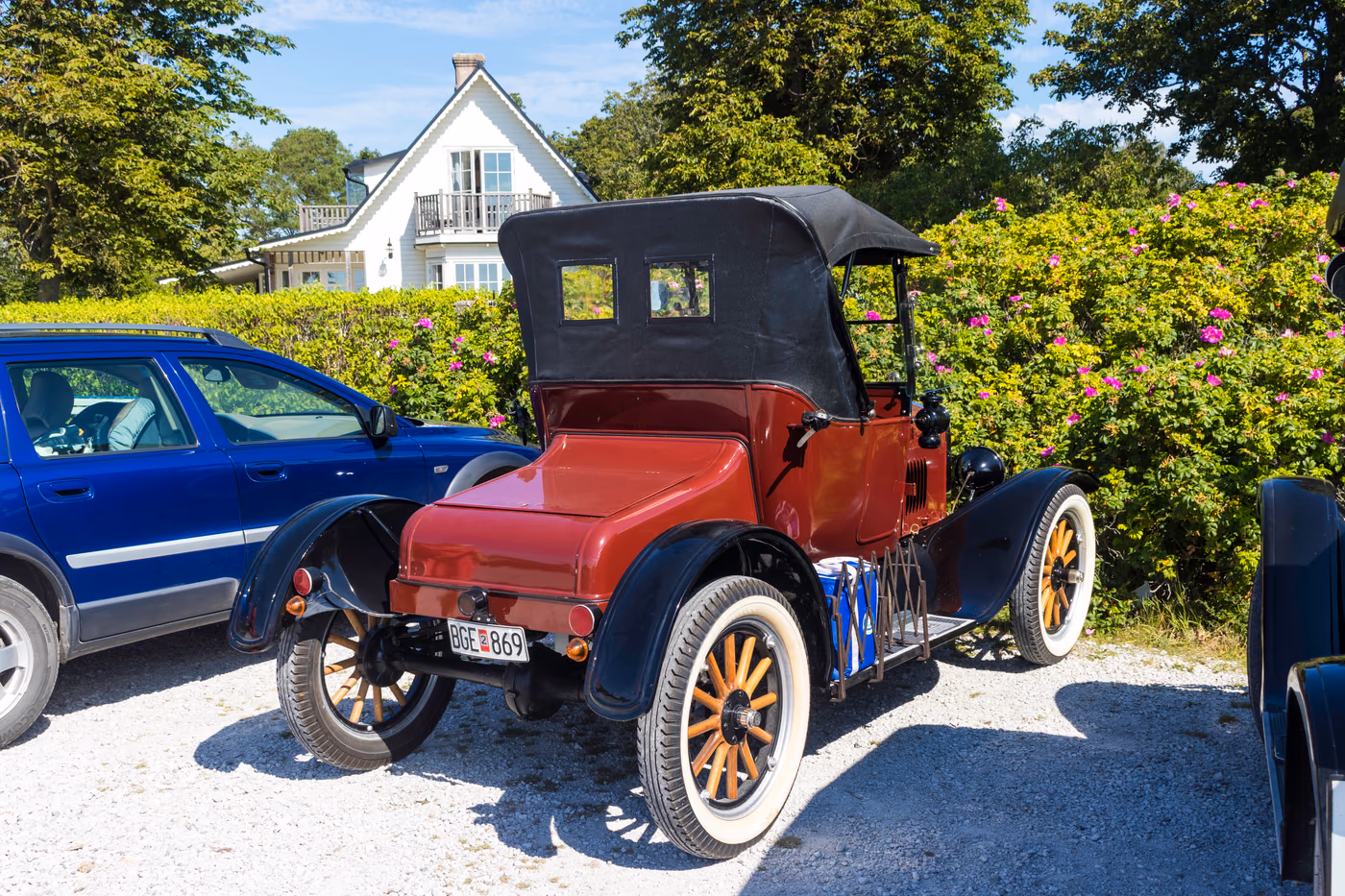 A red 1925 Ford Model T Runabout with a black fabric roof and wooden-spoked wheels, parked in Ljugarn, Sweden